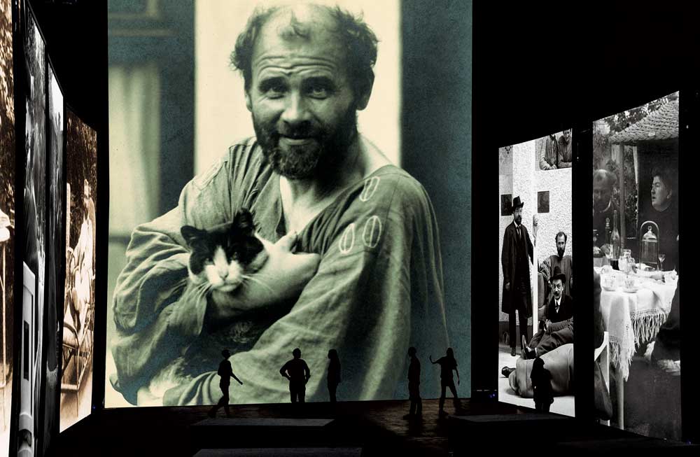 Nello schermo centrale una fotografia di Gustav Klimt che bene rappresenta il carattere eccentrico dell’artista. Sugli schermi laterali foto di gruppo dei secessionisti viennesi.